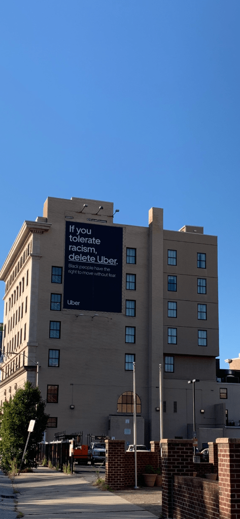 Sign painted on a building that reads: If you tolerate racism, delete Uber. Black people have the right to move without fear.