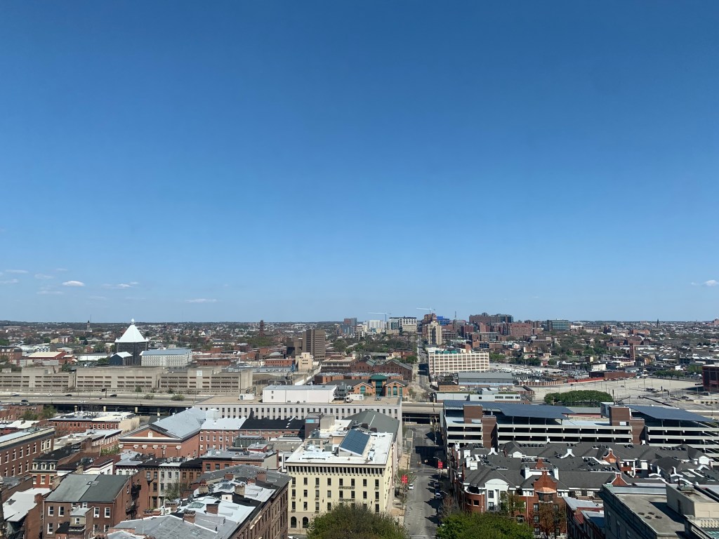The top half of the photo is a clear blue sky and a busy cityscape takes up the bottom half.