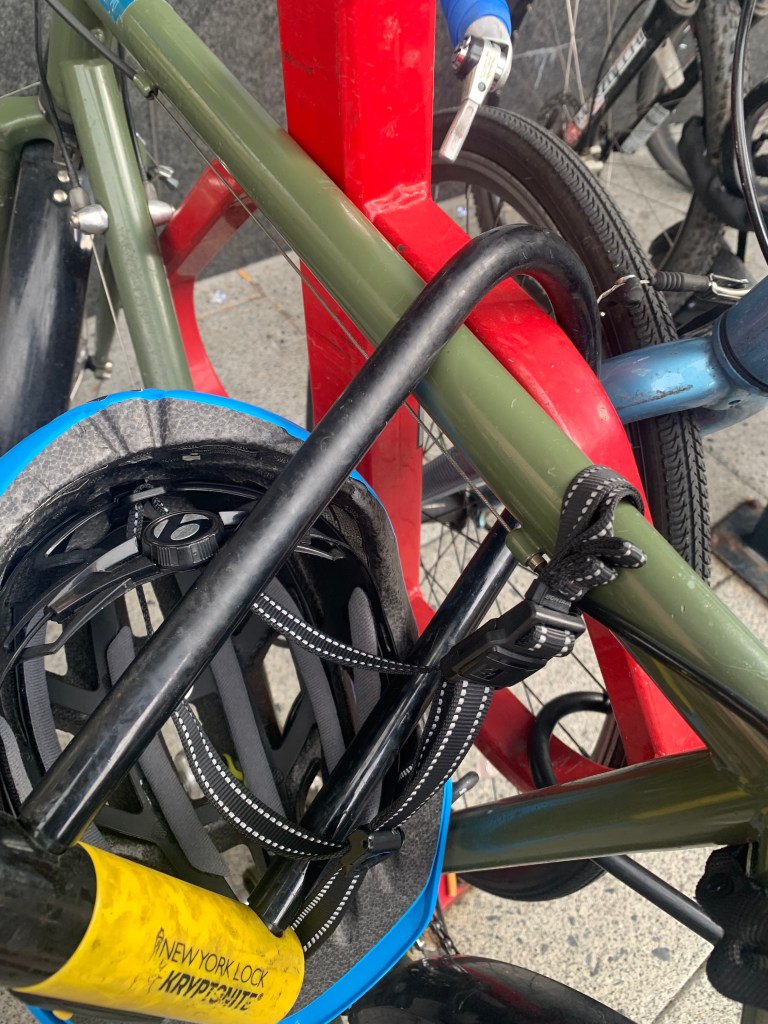 Close up of a black U lock through a red bike rack, a black lock, and a blue bike helmet.